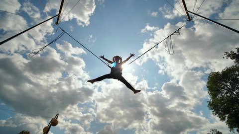 Teenage girl silhouette jumping on the trampoline bungee jumping. Slow motion video.