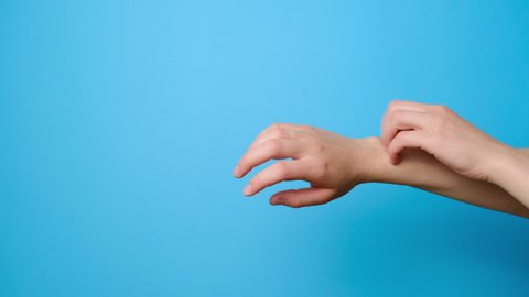 Close up of unrecognizable young woman scratches her hands isolated on blue studio background with copy space. Signs of dermatitis and scabies. Concept skin allergy