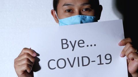 Light shining on Asian woman holding a paper labeled Bye COVID 19 and took off hygienic mask to protect virus on white background. Concept of say goodbye for Corona virus pandemic.
