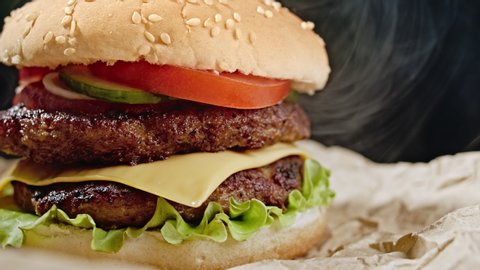 Yummy hamburger, fast food concept. Fresh homemade grilled burger with meat patty, tomatoes, cucumber, lettuce, onion and sesame seeds. Unhealthy lifestyle. Food background. 4k