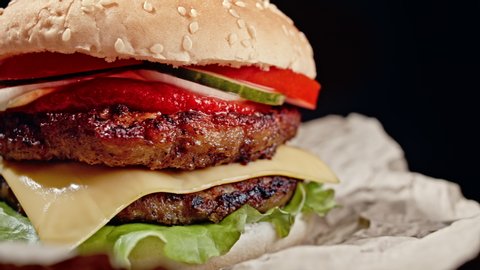 Yummy hamburger, fast food concept. Fresh homemade grilled burger with meat patty, tomatoes, cucumber, lettuce, onion and sesame seeds. Unhealthy lifestyle. Food background. 4k