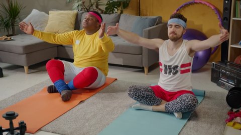 Funny bearded yoga instructor coaching overweight funny young man exercise stretching on mats doing funny meditation together. Sports comedy. Fun.