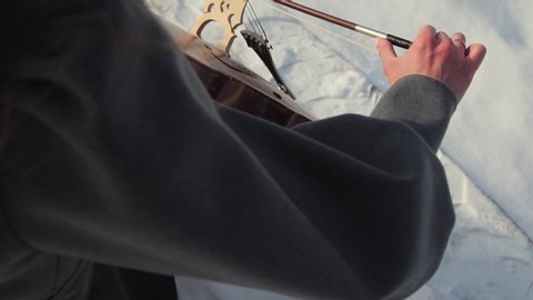 A girl plays the cello in the winter on the street. Snowing. Close-up bow glides over the strings of a musical instrument