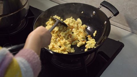 Female hand frying scrambled eggs in wok, top view, homemade food for breakfast