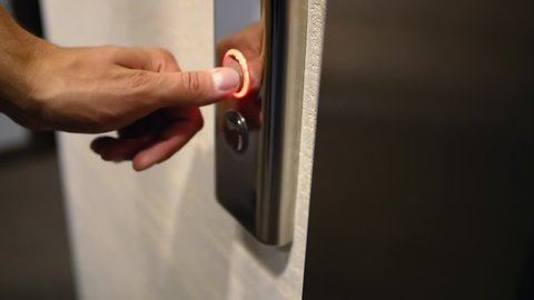 Close-up shot, a male hand presses a metal button to call the elevator after which it glows red. A man calls an lift in a hotel