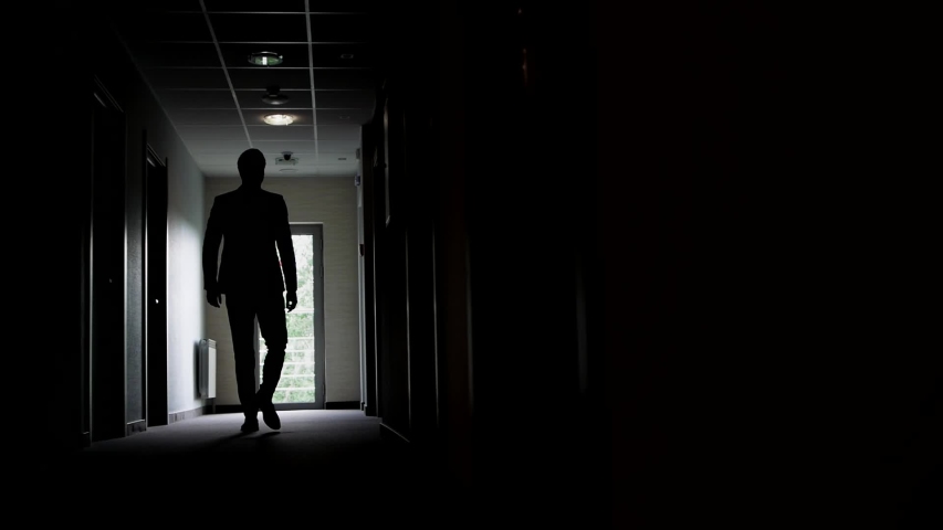 Slow motion, a backlit man walks along the corridor of an office or hotel to the glass doors, then stops and waits. | Shutterstock HD Video #1054661042