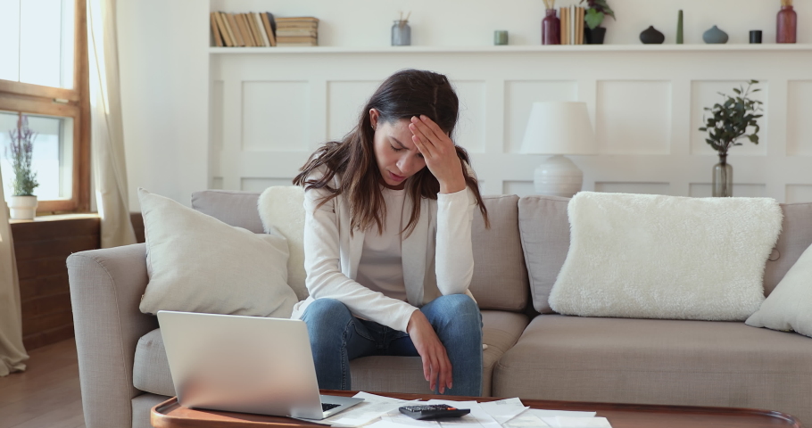 Exhausted frustrated young mixed race girl sitting on sofa at table with paper bills, feeling stressed about bank loan payments, thinking of unpaid taxes, financial problems, money bankruptcy concept. | Shutterstock HD Video #1054663433