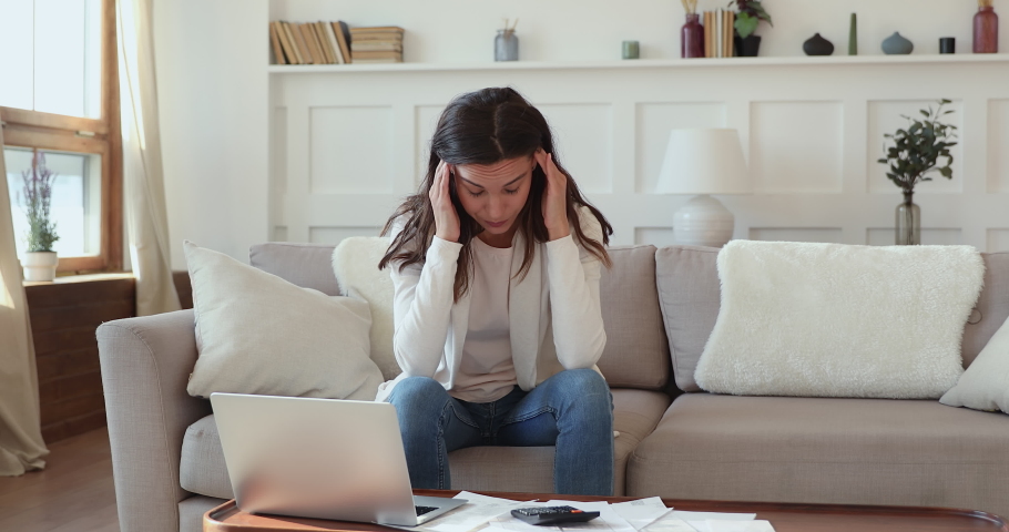 Exhausted frustrated young mixed race girl sitting on sofa at table with paper bills, feeling stressed about bank loan payments, thinking of unpaid taxes, financial problems, money bankruptcy concept. Royalty-Free Stock Footage #1054663433