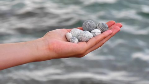 Defocused sea round beautiful gray stones lie in a female hand against background of sea and water. Concept of rest, vacation, relaxation, spa and  meditation. Stones in hand. Slow motion video.