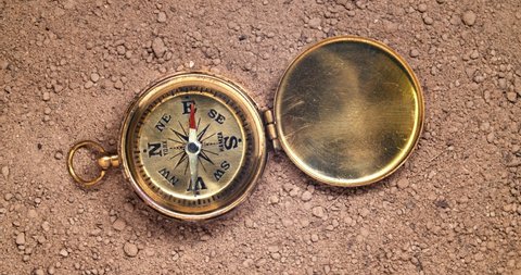 An old golden compass sitting on dirt with the compass arrow spinning wildly. Concept of lost direction, or searching for a path or adventure. 