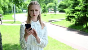 Video portrait of a blonde girl talking a phone in a park. Generic concept of a pretty caucasian woman in sunny weather.