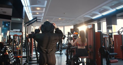 Female athletes in the gym. Tracking shot between the rows of simulators in the gym, a group of girls dressed in black sporty clothes performing different exercises. 4k  slow motion.