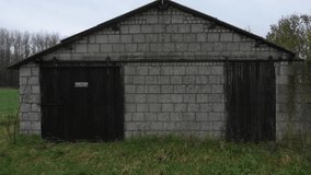 Video that slowly flies over a small stone shed with sturdy wooden doors and a plastic roof
