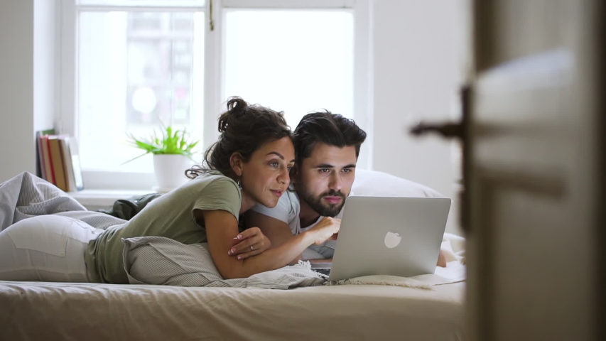Happy married caucasian couple using laptop at home Spbd. man and woman watching movies, browsing internet, searching. concept technology, communication, husband. resting at home | Shutterstock HD Video #1054674050