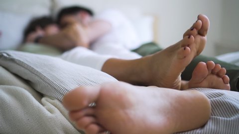 Young American couple is showing love and passion while lying on bed in white room spbd. Blurred view of pretty woman and bearded man have romantic time together, hugging and touching each other. Two
