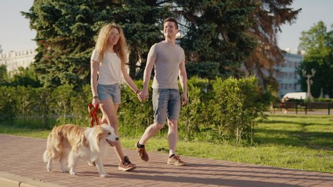 Loving couple man and woman walking with a border collie dog in city park relaxing enjoying warm day outdoors. Social distancing together.People and animals concept. Enjoying summer