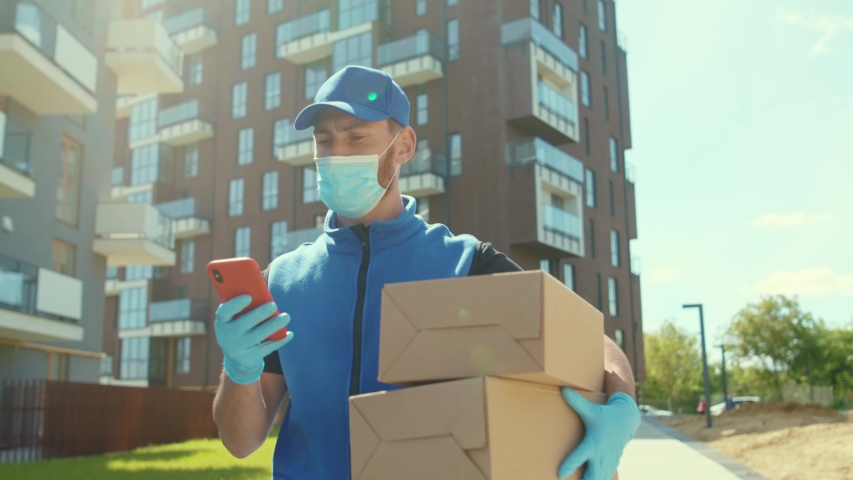 Young delivery man wear mask and gloves holding box use phone walking on street quarantine outdoor shopping package pandemic postman self isolation slow motion Royalty-Free Stock Footage #1054675376