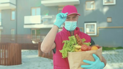 Close up at sunlight courier in uniform wear medical mask and gloves walking holding packet with food delivery worker grocery to house door to door delivery during quarantine slow motion