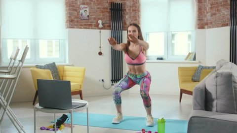 Fit young woman doing workout with online trainer using laptop at home standing in side plank building strong core focused and motivated slow motion