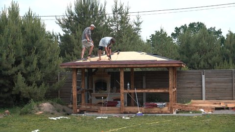 Europe, Kiev region, Ukraine - June 2020: Builders cover the roof with a wooden arbor. Construction of a wooden gazebo. Catopal laying.