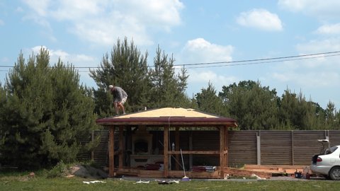 Europe, Kiev region, Ukraine - June 2020: Builders cover the roof with a wooden arbor. Construction of a wooden gazebo. Catopal laying.