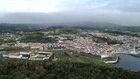 Aerial video of quaint village on the island of Terceira in the Azores with green volcanic hills covered in clouds