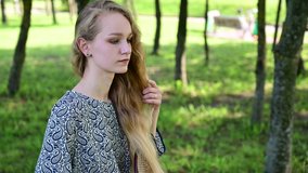 Video Caucasian blonde woman combing her hair in a park. Model posing in clear weather.