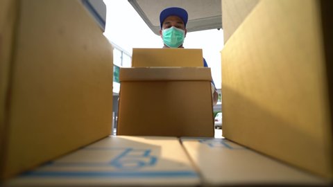 Corona Virus Concept. Asian blue delivery man wearing protection mask and medical rubber gloves mover unloads his cargo van prepare to send to customers. 4k resolution and slow motion shot.