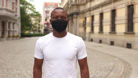 Portrait of a young black man in a black mask on a city street. Protective mask after quarantine, post-quarantine life, new normality, black lives matter