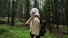 Blonde woman in headphones with backpack in rainy forest