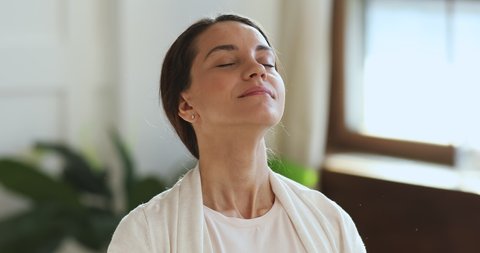 Mindful young biracial woman breathing fresh air, feeling freedom or happiness indoors. Head shot close up peaceful lady meditating, doing yoga relaxation exercises, enjoying weekend time alone.