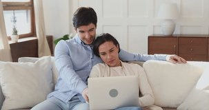 Happy loving mixed race couple using laptop, planning romantic weekend time together at home. Affectionate man cuddling beloved woman, looking at computer screen, shopping online or web surfing.