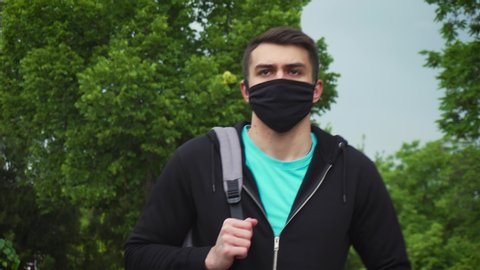 Portrait of young tourist man wearing protective face mask walking in urban park. Stop covid-19 and SARS-CoV-2 infection