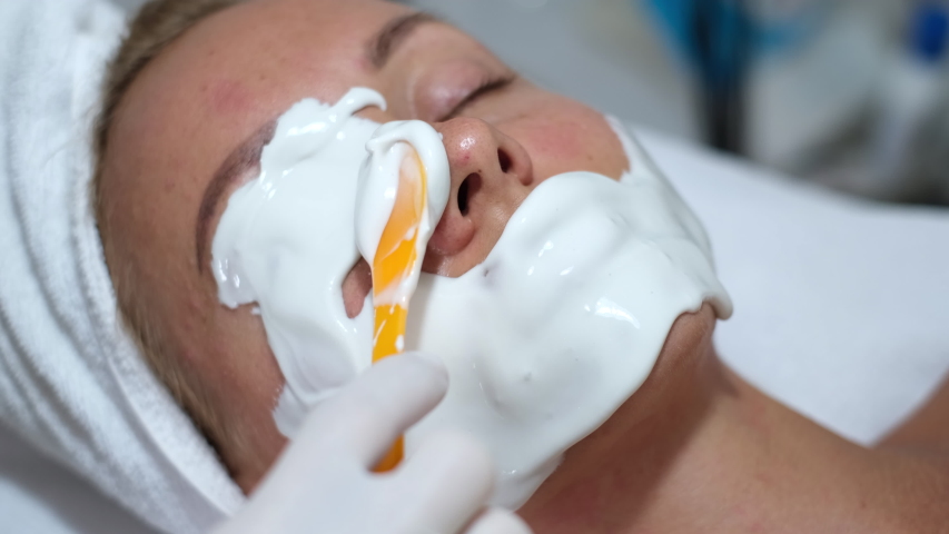 Cosmetologist applies alginate mask with spatula on face of woman. Facial skin and anti-aging treatment. Cosmetology and professional facial skin care.      | Shutterstock HD Video #1054691984