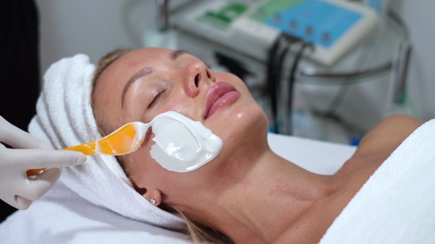 Cosmetologist applies alginate mask with spatula on face of woman. Facial skin and anti-aging treatment. Cosmetology and professional facial skin care.      | Shutterstock HD Video #1054692002