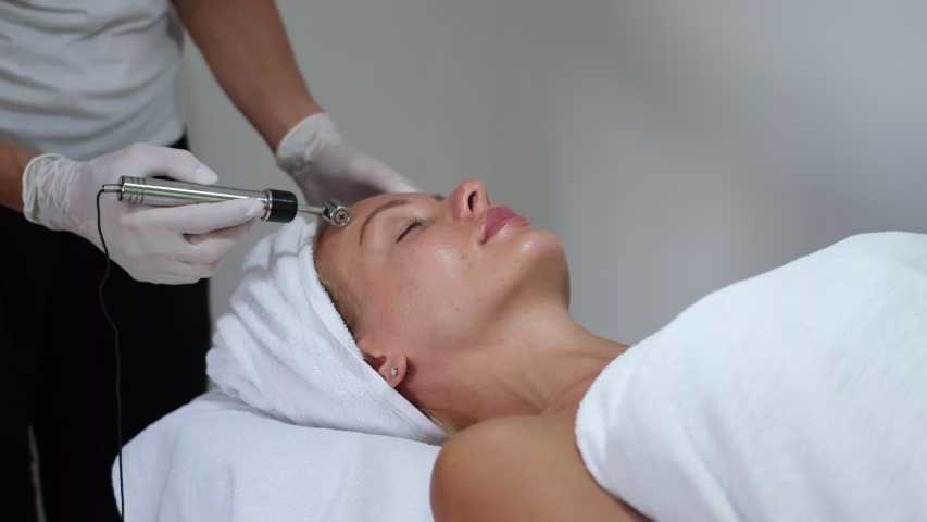 Cosmetology. Woman in clinic receiving stimulating electric facial treatment. Closeup Of Young Female Face During Microcurrent Therapy.   | Shutterstock HD Video #1054692056