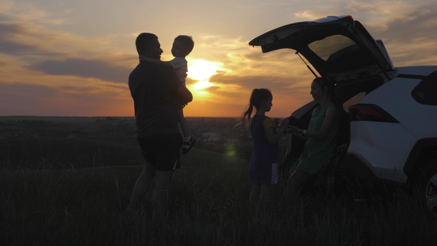 Silhouette the happy family of four people, mother, father and two children are happy sitting in the open trunk of a car at the sunset time. Concept of summer vacation and friendly family.