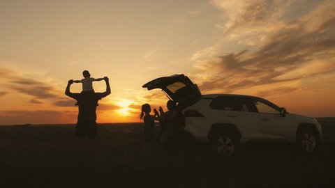 Silhouette the happy family of four people, mother, father and two children are happy sitting in the open trunk of a car at the sunset time. Concept of summer vacation and friendly family.