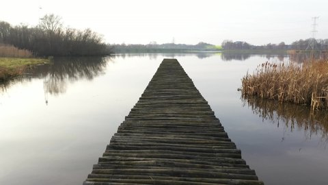 Slowly walking over a large wooden jetty into a lake and flying over the water afterwards