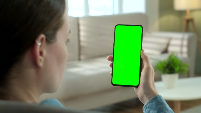 Back View of Woman at Phone with Green Screen for Copy Space. Chromakey Mock Up Without Tracking Markers. 20s Lady Watching Video News on Couch Close up. Tap to Click on Centre of Screen Royalty-Free Stock Footage #1054696007