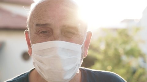 Senior old man is wearing face mask in outdoor. Sun light, flare and elderly senior guy is protecting himself from coronavirus, covid-19