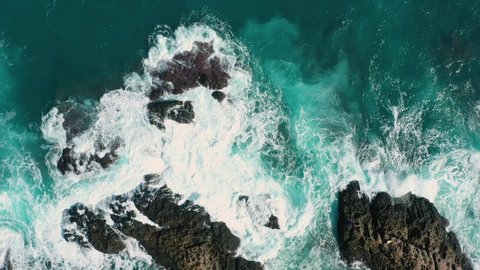 Aerial top view 4k footage by drone of ocean blue waves break on high cliff of a rocky mountain. Danger sea waves on a beach