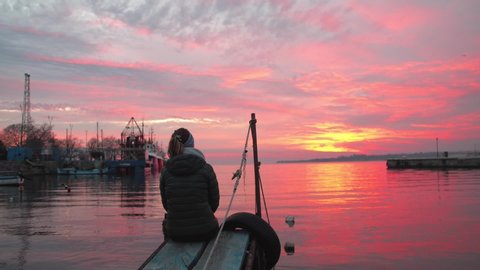 Woman Watching The Beautiful Sunset While Sitting At The Sea Port In Bulgaria - wide shot