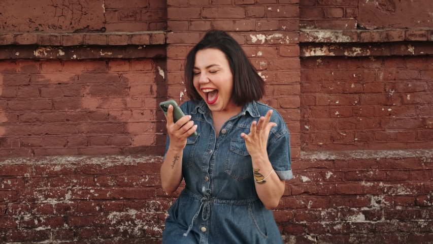 Amazed lucky woman using phone looks and sees the message with a good news. Happy female is surprised, rejoices and  jumps.  Royalty-Free Stock Footage #1054700384