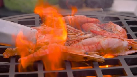 Seafood, barbecue, outdoor cooking, gastronomy, cookery, street food concept. Super slow motion: chef grilling fresh red king prawns on brazier with hot flame at summer local food market - close up