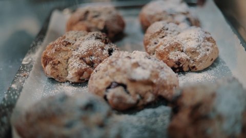 Dusting fruit scones on a tray with icing sugar through a sieve in slow motion.
