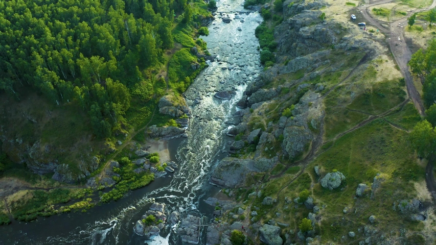 Picturesque valley with a mountain river is a bird's-eye view from a drone. Green meadows and forest on rocky shores. Royalty-Free Stock Footage #1054701551