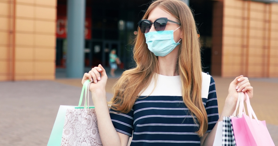 Happy beautiful girl in a medical protective mask on her face, with shopping bags coming out of the store Royalty-Free Stock Footage #1054701743