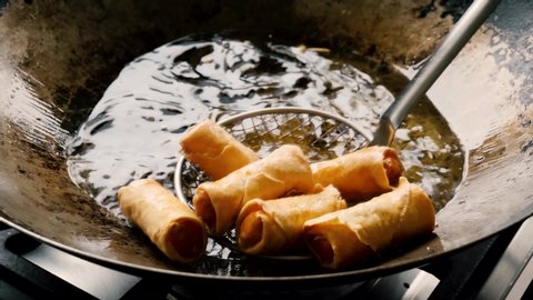 Hot Asian spring rolls are finished frying in steel wok and red with slotted metal mesh scoop, close up static