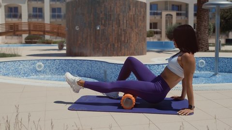 sporty woman stretching and fitness massage with foam roller. Athletic female massaging legs on yoga mat with foam roller outdoors. 